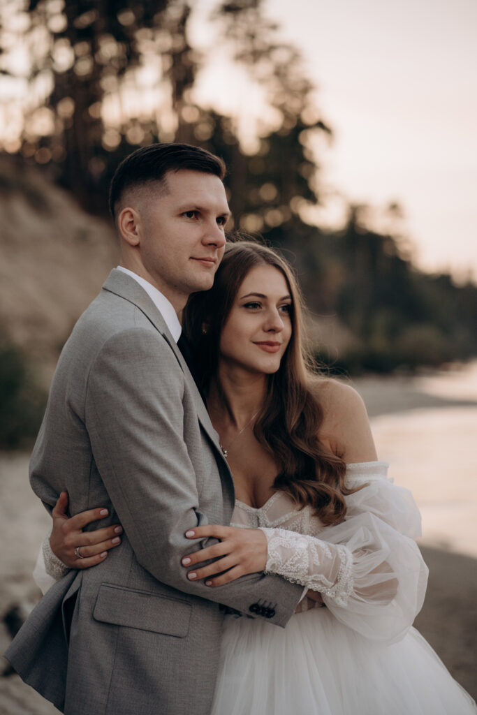 Side view of bride wearing white dress, groom wearing costume having wedding ceremony. Happy couple getting marries, smiling, looking forward. Concept of wedding and happiness.